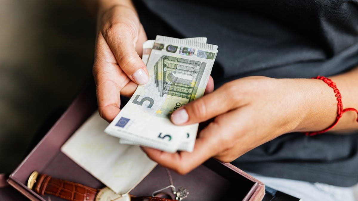 Close-up of hands counting euro notes above a wristwatch in a box.